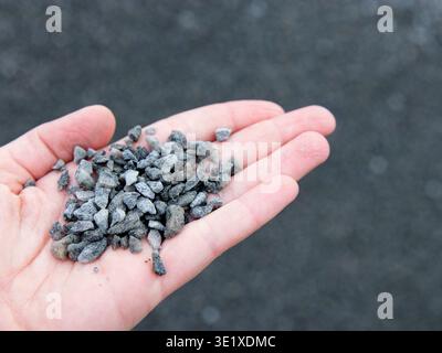 Hand holding small pieces of gray gravel against a blurred dark background, showcasing the texture and size of the stones in a natural setting Stock Photo