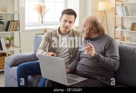 Adult son teaching his mature father how to use laptop computer, explaining something  Stock Photo