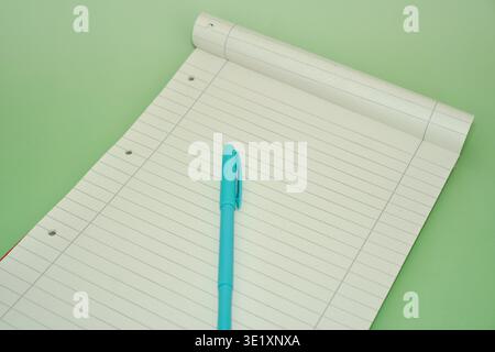 Top view of an open white lined notebook with a teal or cyan pen placed on it. Minimalist workspace concept on a light green background. Clean template for education, business planning, to-do lists, and office stationery. Lined Notepad with Cyan Pen on Pastel Green Background. High quality photo Stock Photo