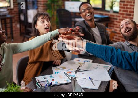Male and female colleagues bonding through cheerful gesture, fostering positivity and teamwork in modern workspace. Professional business team smiling and celebrating new chapter for startup company. Stock Photo