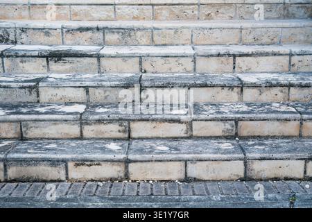 Full view of outdoor stone steps with weathered surfaces and dark moisture stains next to a patterned brick walkway in the city. Stock Photo