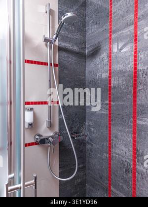 Modern shower cabin interior with chrome faucet, handheld showerhead, gray textured wall tiles and red mosaic accents, contemporary bathroom design Stock Photo