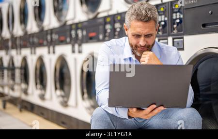 Laundry overload for busy businessman doing housework. Money laundering. Busy man working on laptop at laundry. Overloaded employee multitasking Stock Photo