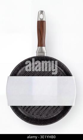 Mockup of a round black grill pan with a wooden handle and a blank white paper sleeve, top view. Stock Photo