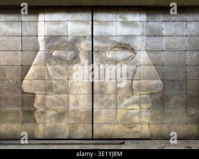Two faces look in opposite directions on the outside metal doors to the loading garage of an exhibition hall in Prague. Stock Photo