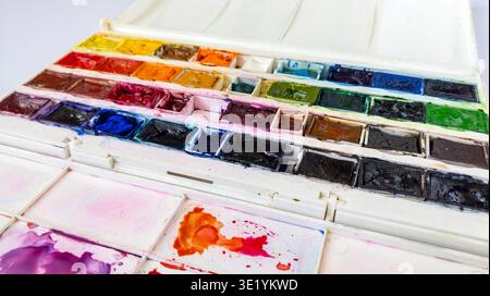 Open plastic box containing a set of used professional watercolor paints in pans on a white background. Close-up of a collection of watercolor paints Stock Photo