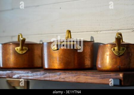 Vintage antique copper pots on a rustic wooden shelf over a hundred years old and in use. Quality craftsmanship Stock Photo