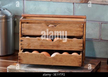 Rustic wooden antique egg storage box filled with fresh eggs with chicken feed container and green tile in background Stock Photo