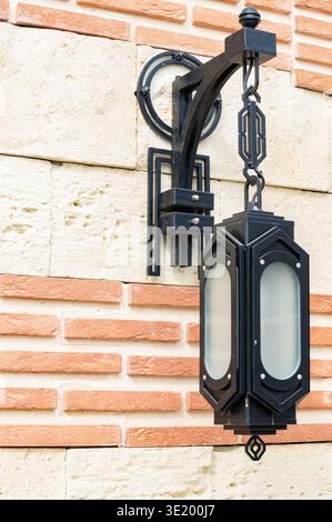A lamp hanging from a wall. The lamp is black and white. The wall is made of bricks Stock Photo