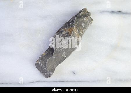 A single rough gray stone rests on a white marble surface with subtle veining Stock Photo