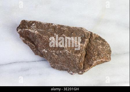 Rough textured brown rock with white mineral veins on a white marble surface Stock Photo