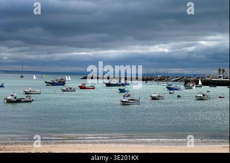 Colorful fishing boats anchored in Cascais harbor, Portugal, under dramatic cloudy skies along the Atlantic coast. Stock Photo