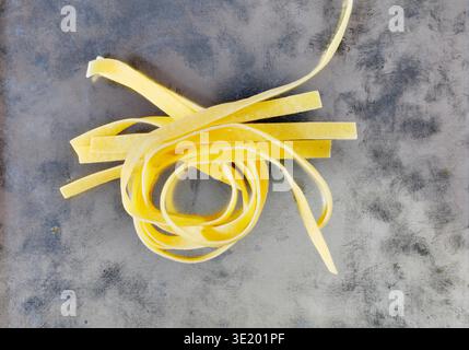 Uncooked dried fettuccine pasta on gray  background ready for cooking , long flat pasta served with variety of sauces Stock Photo