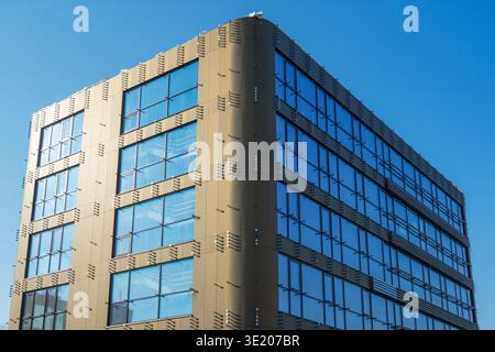 Modern unfinished office building with large glass windows and geometric facade panels under clear blue sky, showcasing contemporary architecture Stock Photo