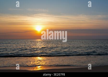 Golden sunset over the Baltic Sea with calm waves rolling onto sandy beach and warm reflections on the water Stock Photo