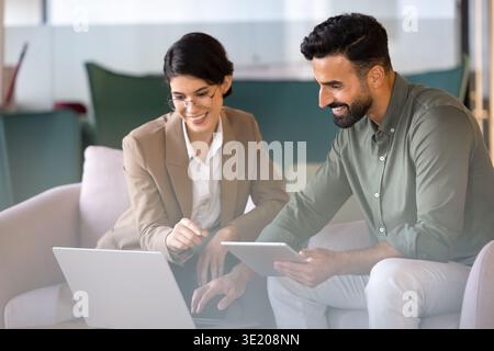 Team members collaborating, analyzing business data using laptop and tablet Stock Photo