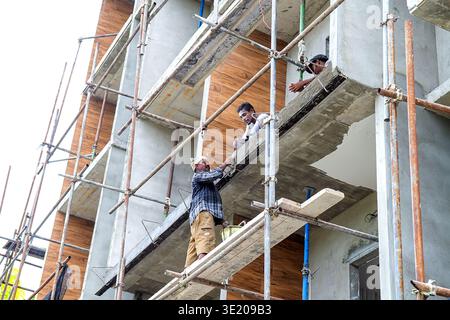 Maldives, Thoddoo - 22 Feb 2022: Two male laborers with dark skin in casual work attire engaged in building finishing work, one standing with brush ap Stock Photo