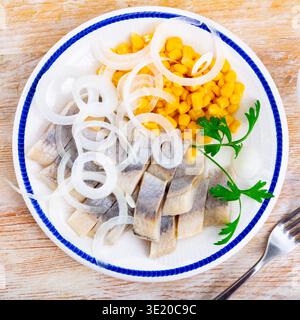 Sliced pickled herring fillet with corn and onions on plate Stock Photo