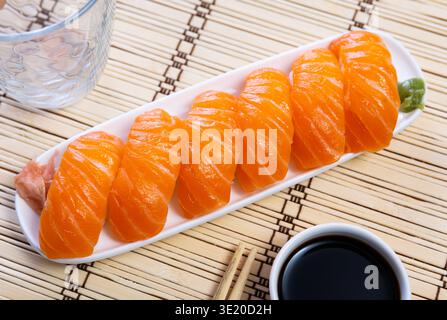 Blue rectangular ceramic plate of delicious salmon nigiri with soy souse on bamboo mat. Stock Photo