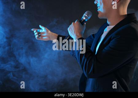 Happy presenter with microphone performing on dark background with smoke, closeup Stock Photo