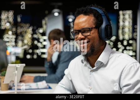 Close up of smiling software developer wearing headphones doing code testing. Joyous african american man in tech startup office designing and debugging applications, listening music Stock Photo