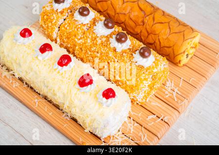 Three Delicious Swiss Roll Cakes with Cream Frosting and Cherries on Wooden Board Stock Photo