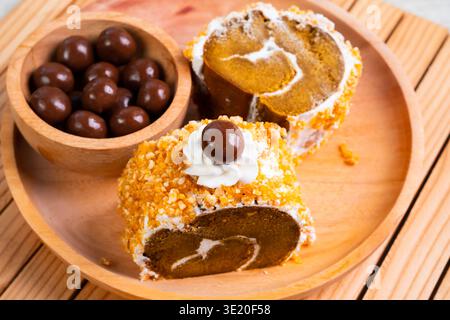 Close Up Dessert Roll with Cream and Chocolate Balls on Wooden Plate Top View Stock Photo