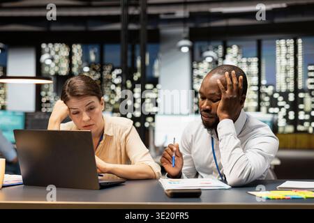 Multiracial team of employees in office feeling upset after missing project deadline, using laptop. Teamworking colleagues analyzing company revenue on notebook, saddened by poor quarterly sales Stock Photo