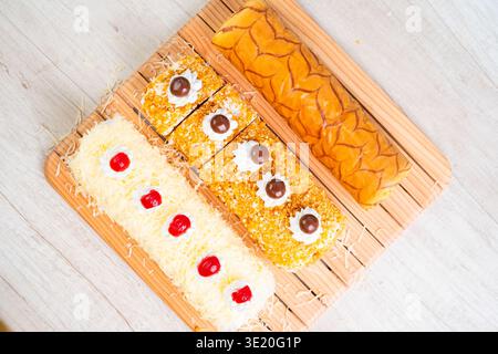 Assorted Swiss Roll Cakes With White Cream Topping And Chocolate Drizzle On Wooden Board With White Table Background Overhead Shot Stock Photo