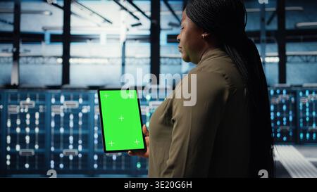 Admin with isolated screen tablet in data center implementing advanced power management solutions. Employee using chroma key device to oversee server hub, reducing energy consumption, camera A Stock Photo
