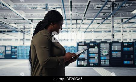 Developer in data center using tablet to upgrade systems for increase in clients workload capacity. IT expert in server farm configuring hardware, improving data processing speed, camera A Stock Photo