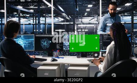 Female technician and coworker in data center review AI diagnostics on isolated screen PC. IT expert and colleague optimize artificial intelligence systems using chroma key computer, camera A Stock Photo
