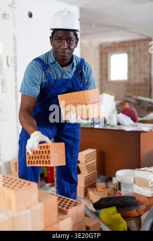 Builder in overall and hardhat carrying bricks in apartment Stock Photo