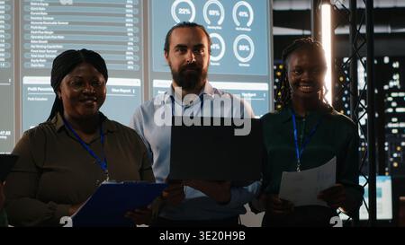 Portrait of team members discussing insight details and progress on a new project, night time corporate meeting for multinational company. Staff informed about marketing developments. Camera B. Stock Photo