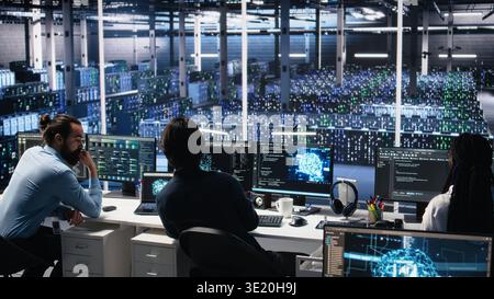Server room system administrators using AI to review infrastructure diagnostics. IT professionals in data center analyzing performance data using artificial intelligence technology, camera A Stock Photo