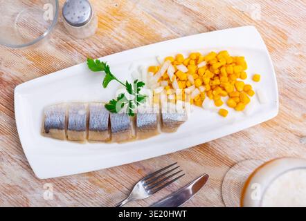 Sliced pickled herring fillet with corn and onions on plate Stock Photo
