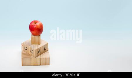 A conceptual still life image featuring natural pine wood blocks that form the word 'GOAL'. A vibrant red apple sits at the peak of the pyramid struct Stock Photo