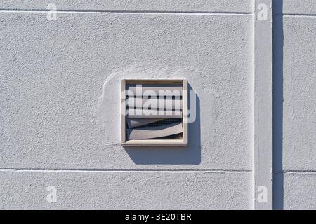 White textured exterior wall with small square ventilation grille casting shadow in sunlight highlighting architectural details and light contrast. Stock Photo