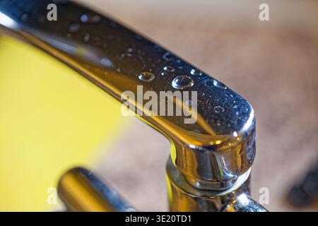 Shiny metal faucet handle with water droplets reflecting light and surface textures. The image highlights water, metal, and reflections in a close per Stock Photo
