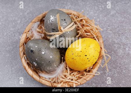 Easter eggs in wicker basket with yellow egg and feathers Stock Photo