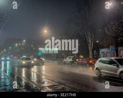 BELGRADE, SERBIA - DECEMBER 7, 2025: Night traffic in Belgrade, Serbia, on heavy rain, with two damaged cars stopped in the roadway. Wet asphalt and p Stock Photo