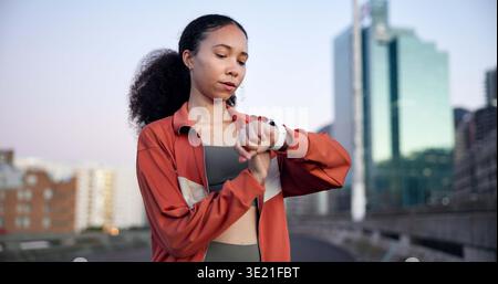 Woman, fitness and smart watch with timer in city for break, monitor or check heart rate on bridge. Gen z girl, runner and stopwatch with iot clock Stock Photo
