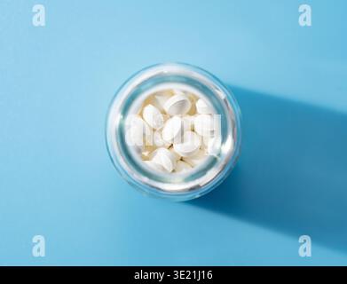Top view of white pills or supplements in a glass bottle on a blue background Stock Photo