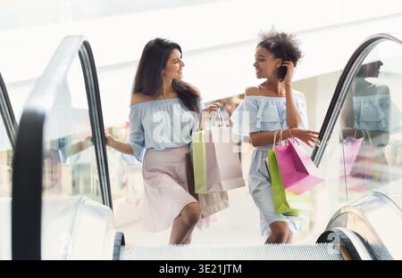 Two multiethnic women on escalator in shopping mall Stock Photo