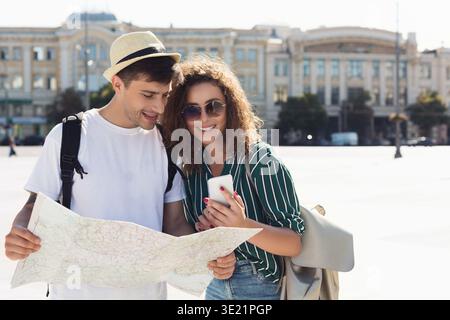 Couple of tourists checking location in smartphone and paper map Stock Photo
