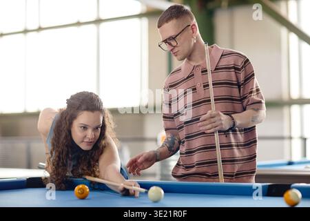 Young Woman Playing Billiards While Young Man Observing Stock Photo