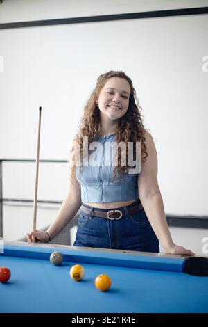 Vertical of Portrait of Young Adult Woman Smiling While Playing Billiards Stock Photo