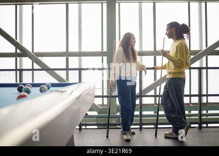 Young Woman and Young Man Chatting While Playing Billiards Indoors Stock Photo