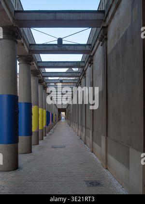 Long perspective view of a covered outdoor corridor with concrete columns, steel beams overhead, and colorful wrapped sections on pillars, creating st Stock Photo
