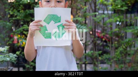 Child holding paper with recycle sign outdoor in a park with copy space. Earth day and ecology concept. Boy holding paper recycling, Recycling concept Stock Photo